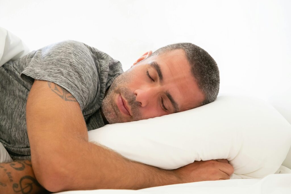 GABA for Sleep A man in a gray shirt, sleeping soundly on his side, with white sheets and pillows: GABA for Sleep