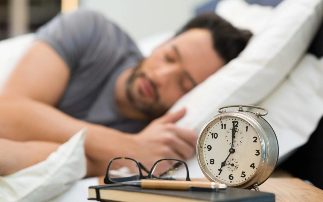 View of a man sleeping in his bed with a view of a clock, letters, and his book