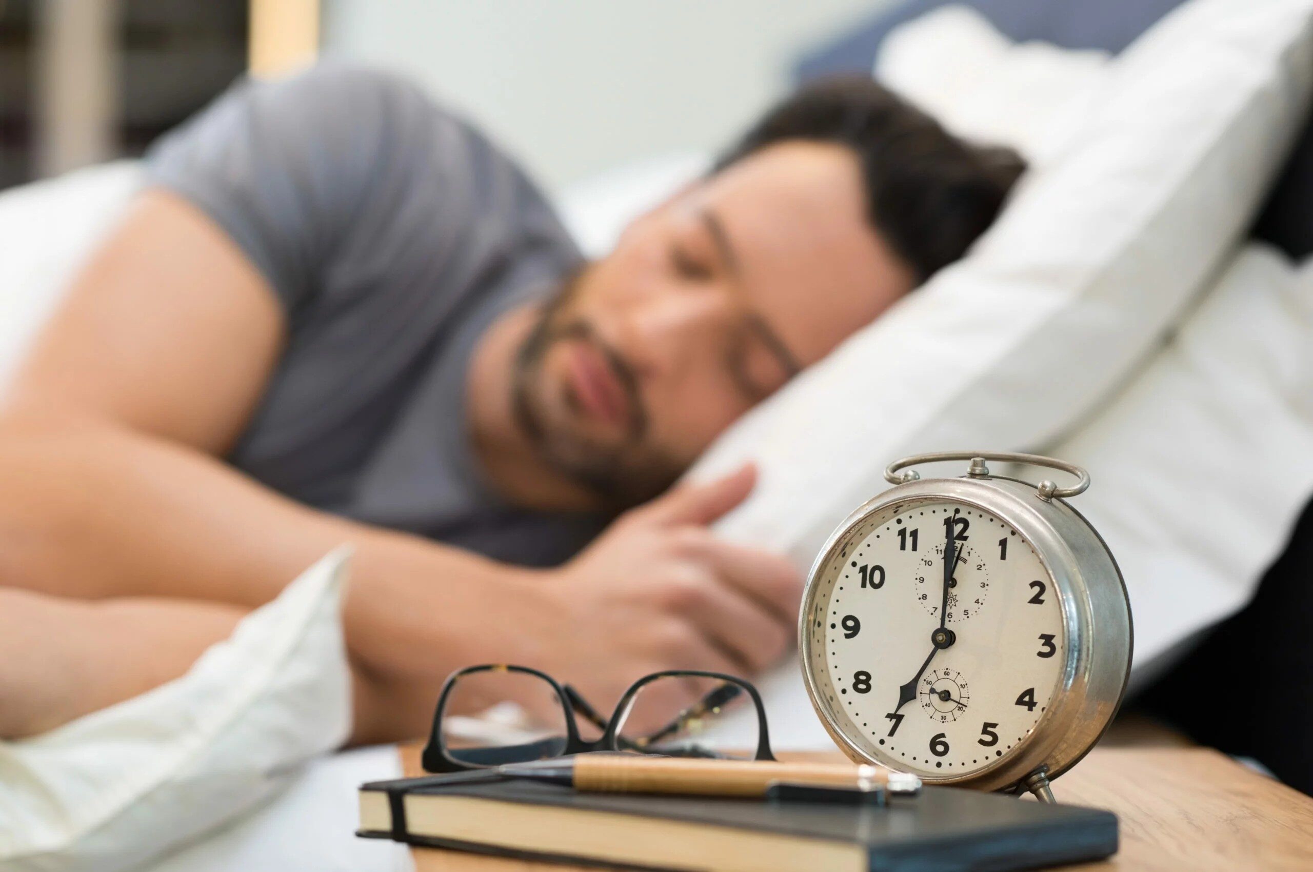 View of a man sleeping in his bed with a view of a clock, letters, and his book
