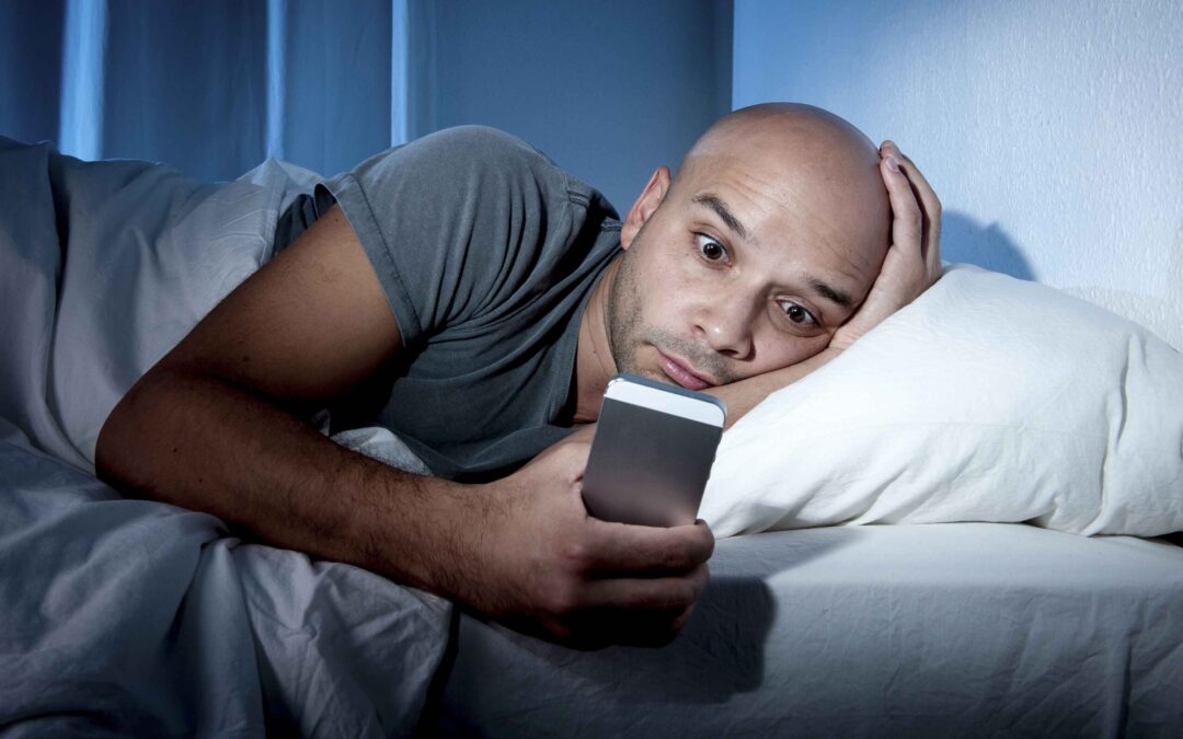 man in his bed unable to sleep looking at his cell phone screen