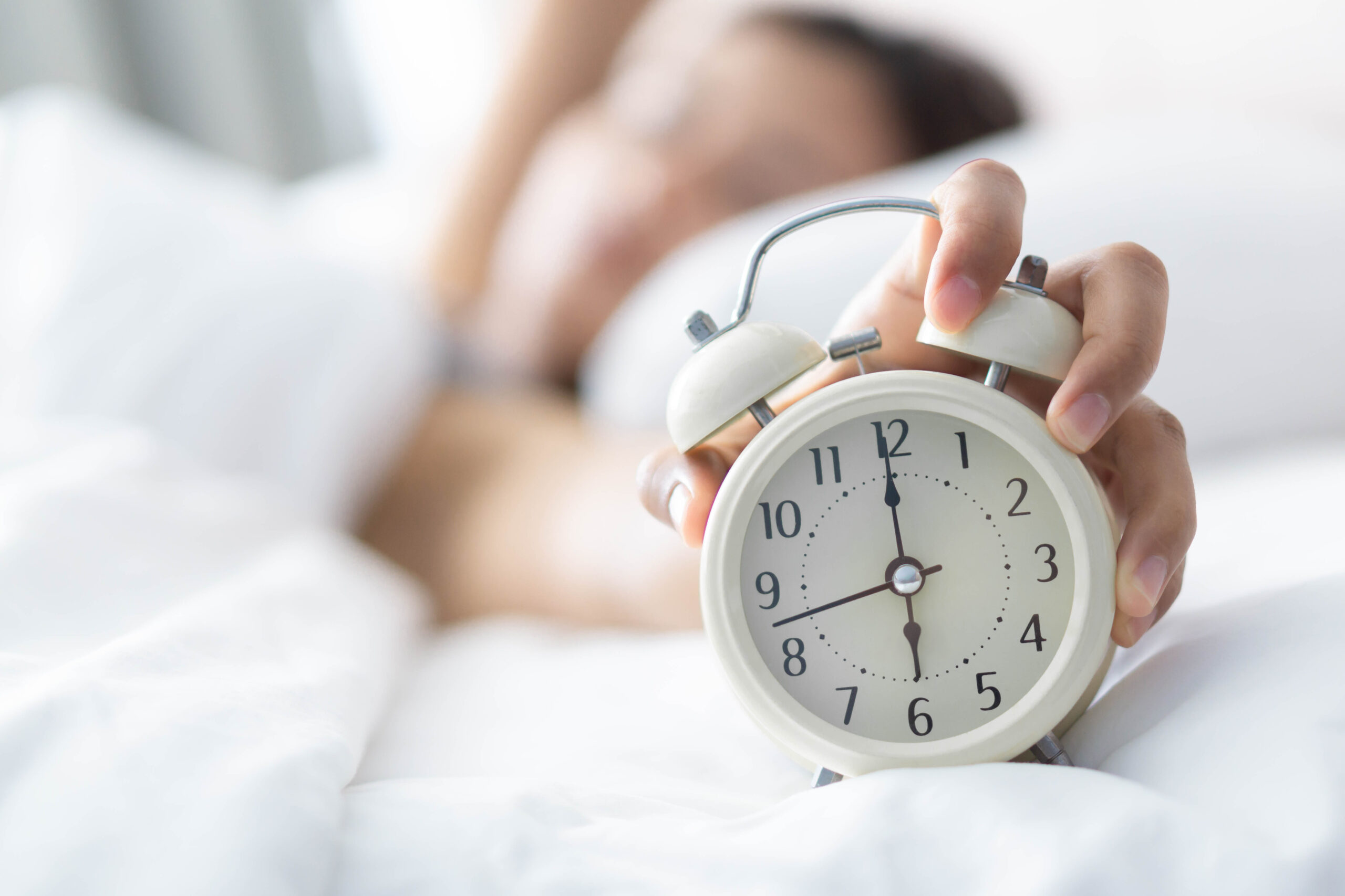 Closeup woman sleeping on bed and hand holding alarm on clock, T person in bed with alarm clock in hand ready to start their day