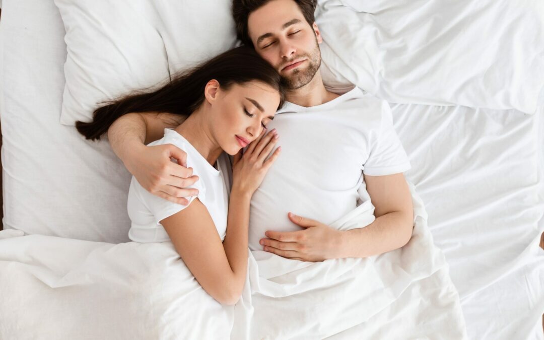 husband and wife in their bed with white sheets sleeping embraced