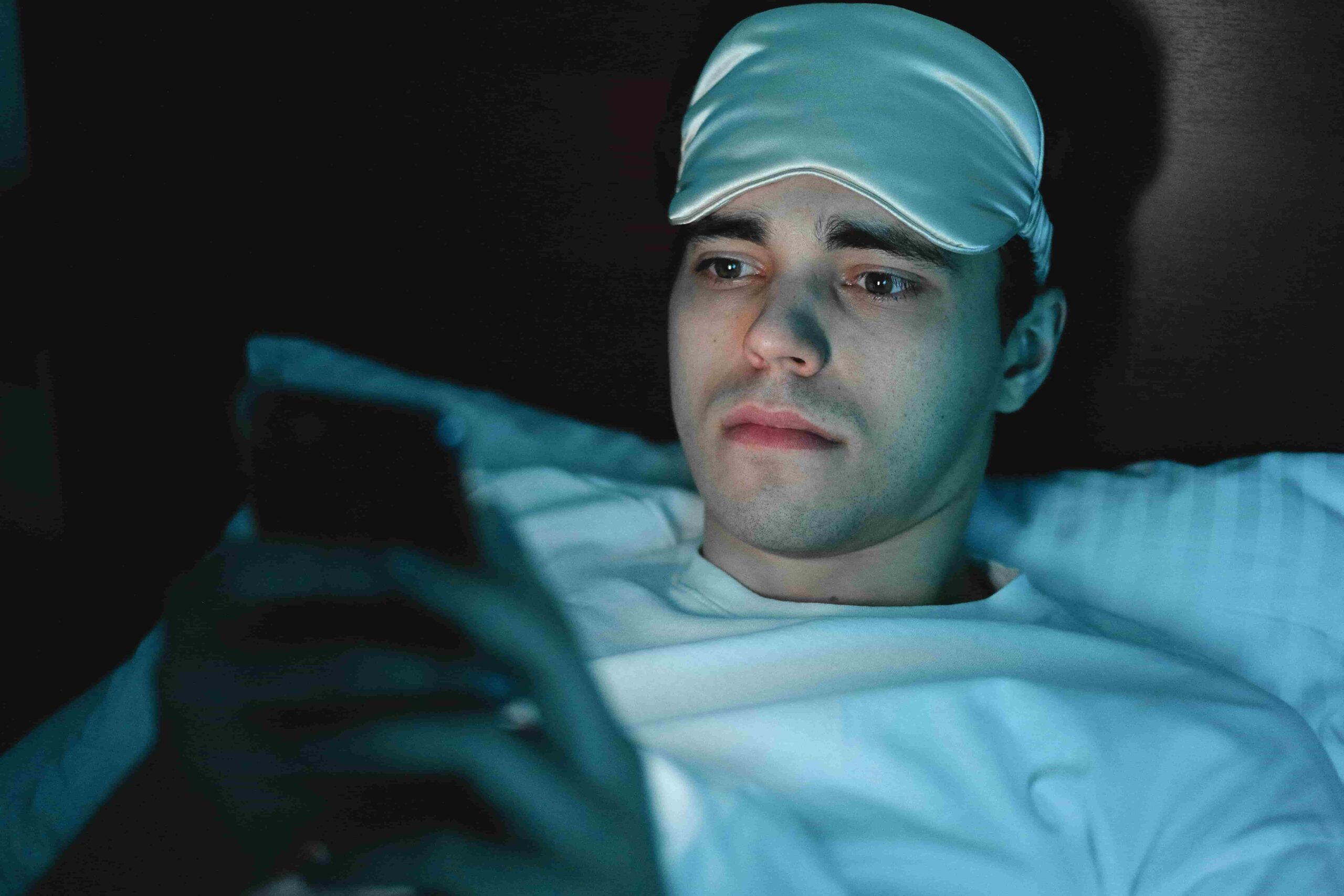 man with insomnia in his bed looking at his phone