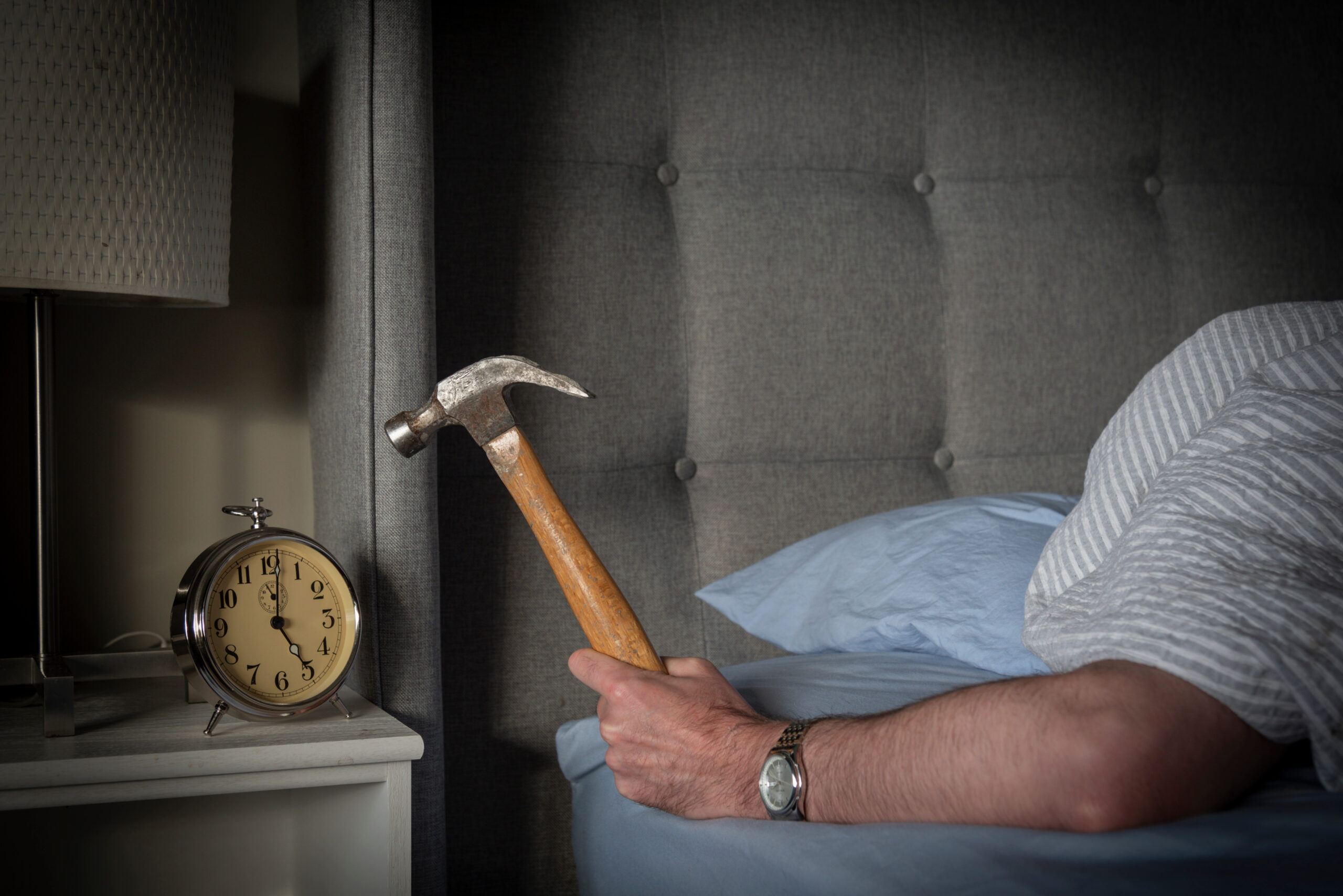 Man trying to sleep in his room hitting his alarm clock with a hammer